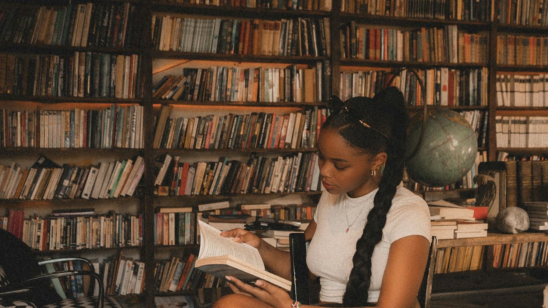 Kenyan student studying with a book in a library surrounded by bookshelves